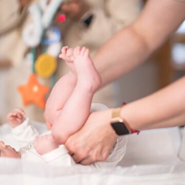 Newborn baby cradled in the arms of caregivers, tiny feet visible on a white blanket