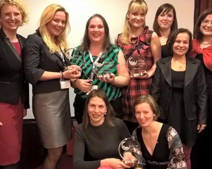Group of women in business attire posing with clear crystal trophies at an awards event.