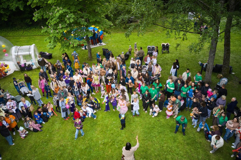 Crowd of families at an outdoor park festival, with a balloon-filled inflatable play area on the left.