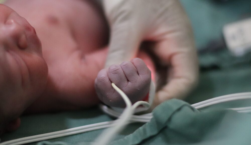 Medicinos darbuotojas laiko neišnešioto naujagimio rankytę intensyviosios terapijos skyriuje.