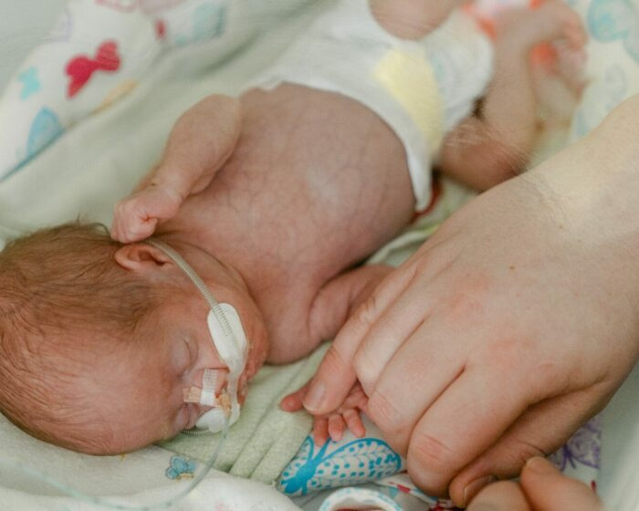Mama ligoninėje švelniai laiko neišnešiotą naujagimį ant krūtinės.