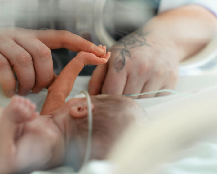 Tėvų rankos švelniai liečia neišnešioto naujagimio rankytę inkubatoriuje